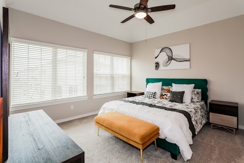 A bedroom with a bed, bench, and a ceiling fan.