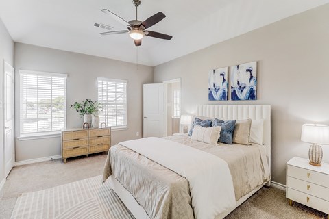 A bedroom with a large bed, a ceiling fan, and a nightstand with a lamp.