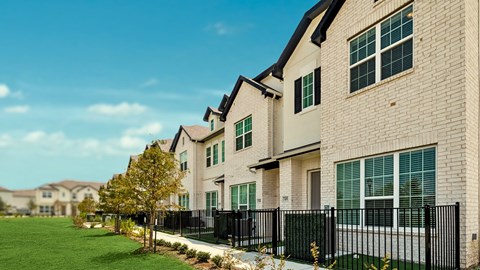 A row of houses with black fences and green lawns.