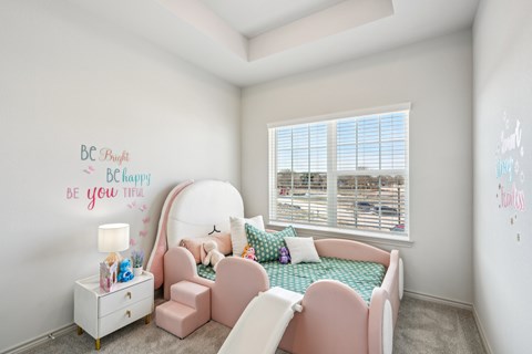 A child's bedroom with a pink chair and a bed with a green blanket.