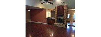 an empty living room with a brick fireplace and wooden floors
