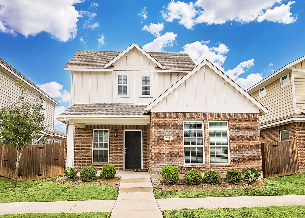 a brick house with white siding and a wooden fence