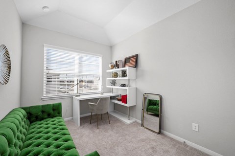 A room with a green couch, desk, and chair.