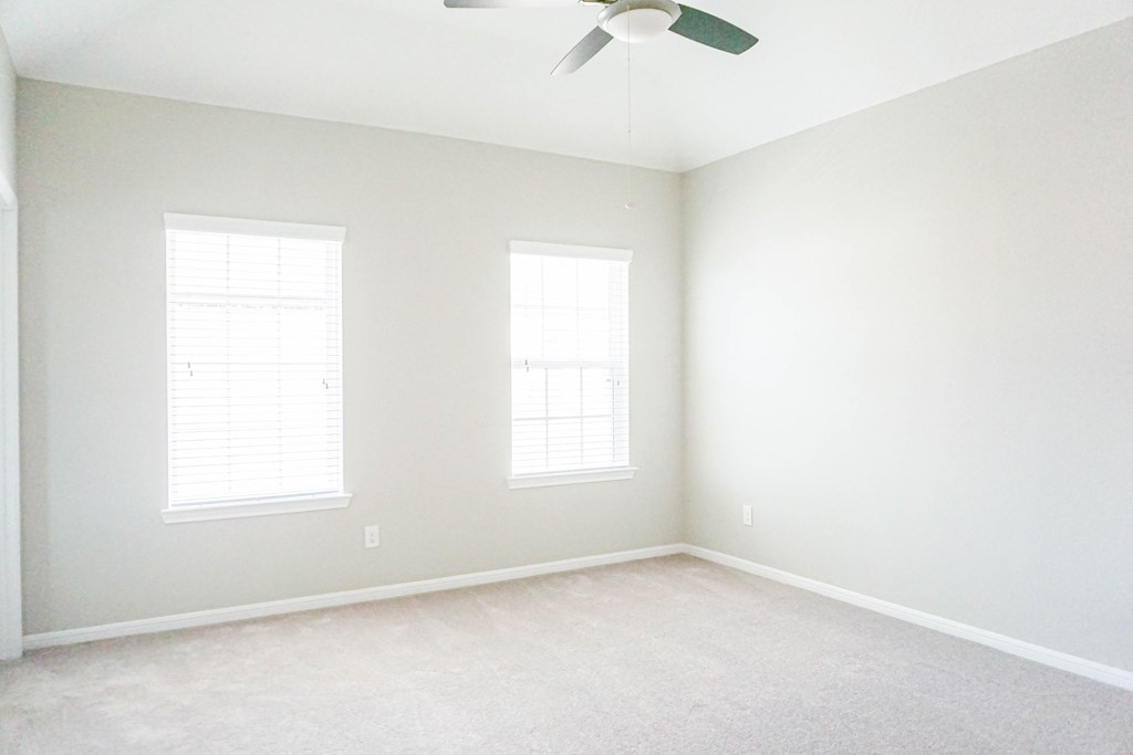 an empty room with two windows and a ceiling fan