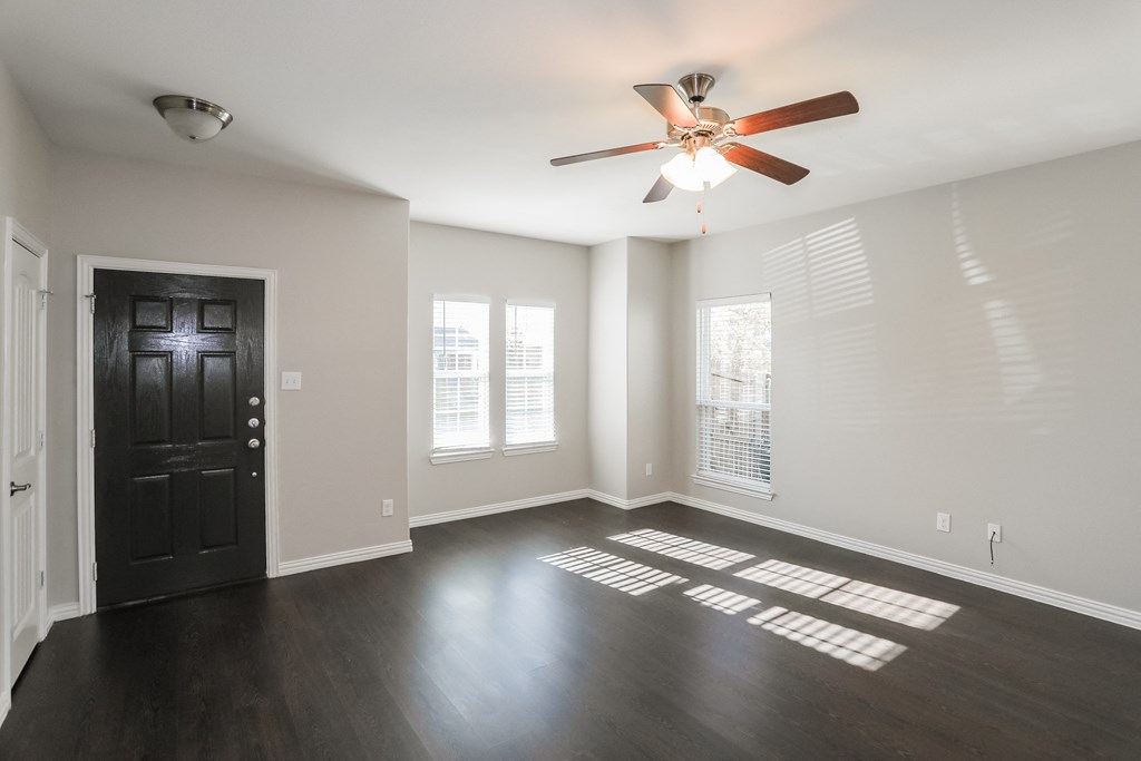 an empty living room with a ceiling fan and windows