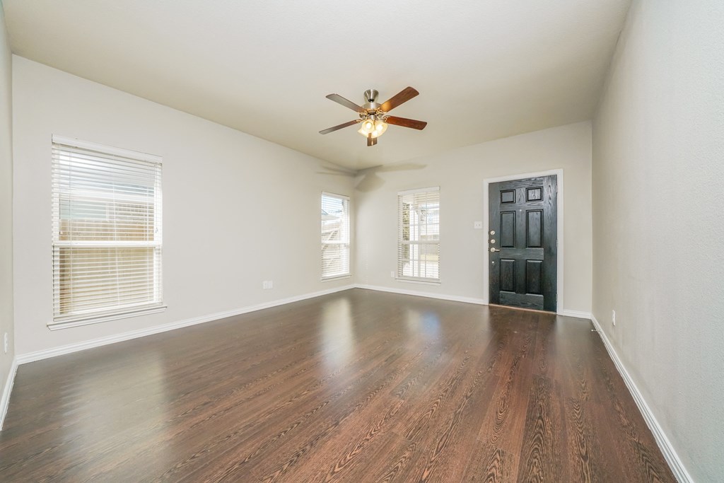 an empty living room with wood floors and a ceiling fan