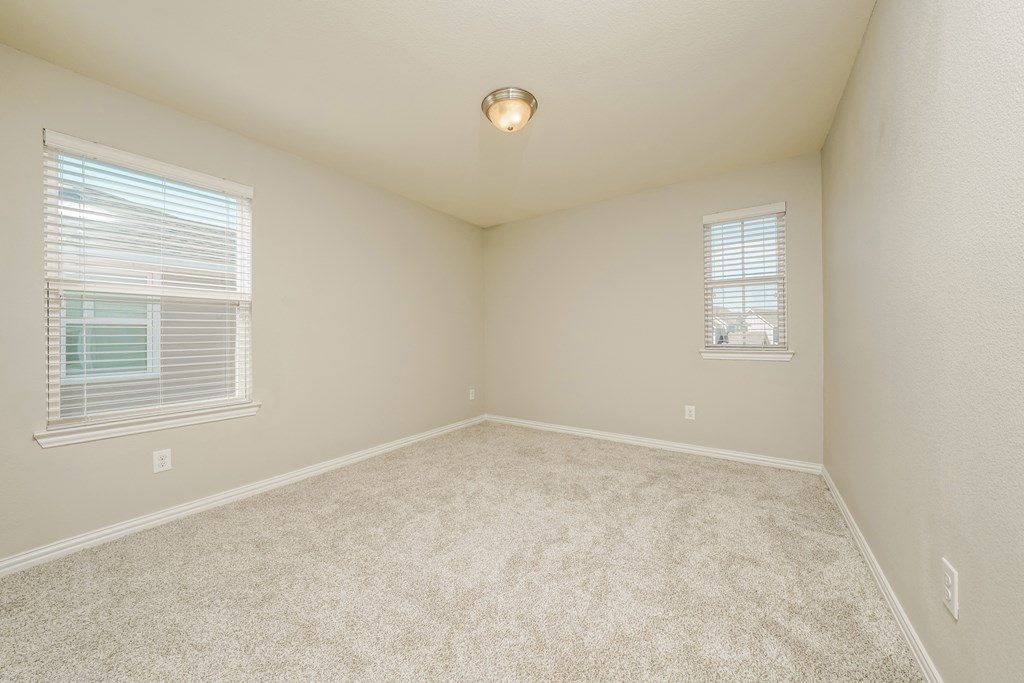 an empty bedroom with two windows and a carpeted floor