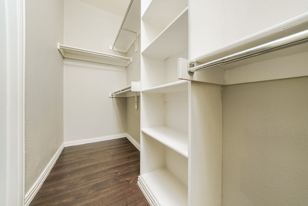 a walk in closet with white shelves and a wood floor