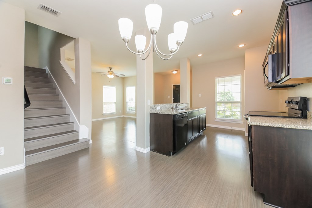 an empty living room with a staircase and a kitchen and a chandelier