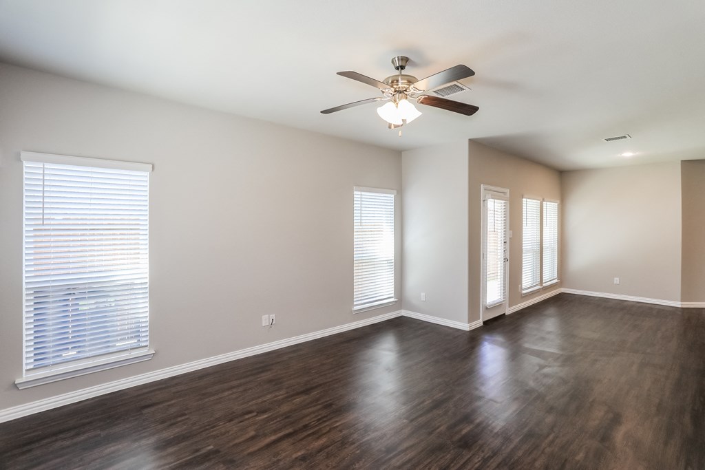 an empty living room with a ceiling fan and windows