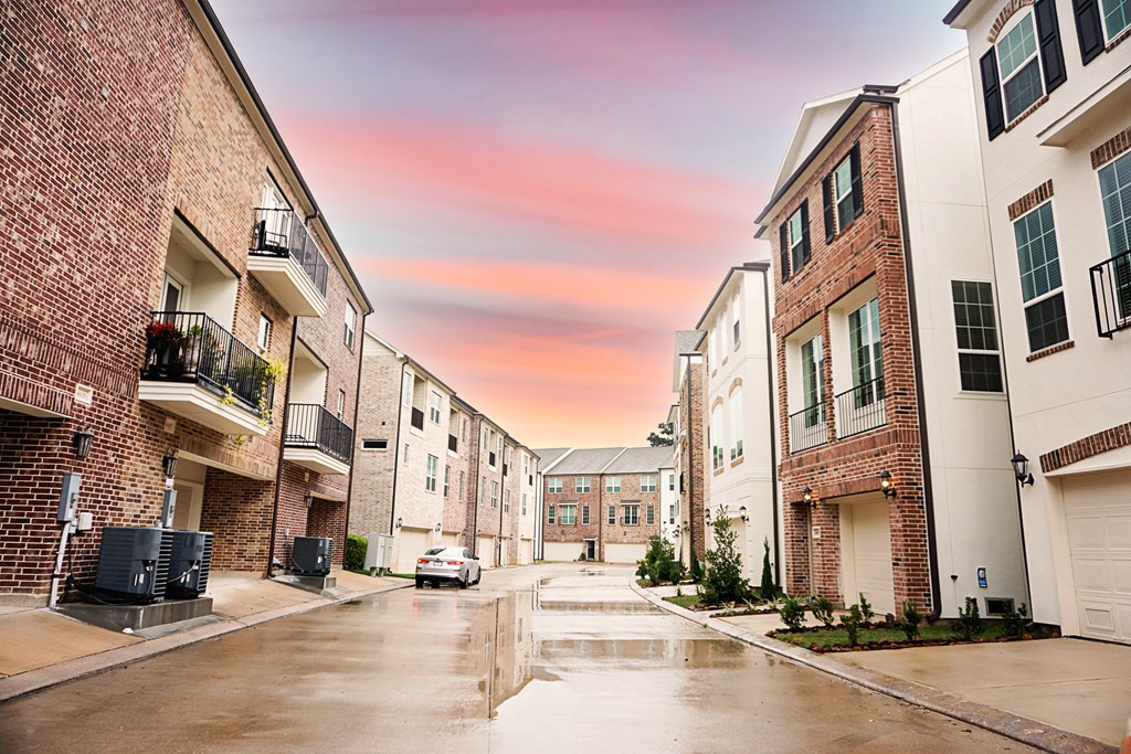 a rainy street with brick buildings and a pink sky