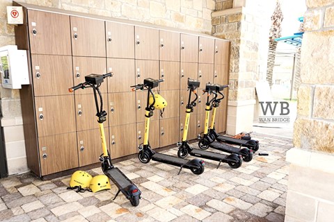 A row of yellow scooters are parked in front of a wooden wall.