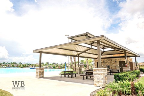 A pavilion with a stone pillar and a bench is located next to a pool.