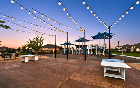 A playground with a table and chairs under string lights.