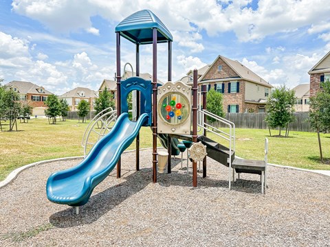 a playground with a slide and other toys in a yard with houses in the background