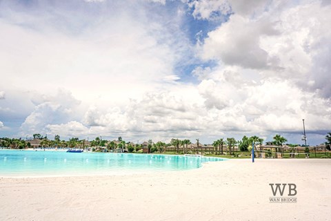 A beach with a pool and palm trees in the distance.