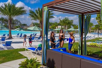 A group of people are standing under a blue and white striped awning at a poolside.
