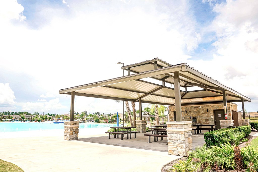 A pavilion with a stone pillar and a bench is in front of a pool.