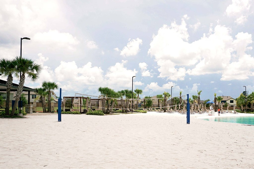 A sandy beach area with a pool and palm trees.