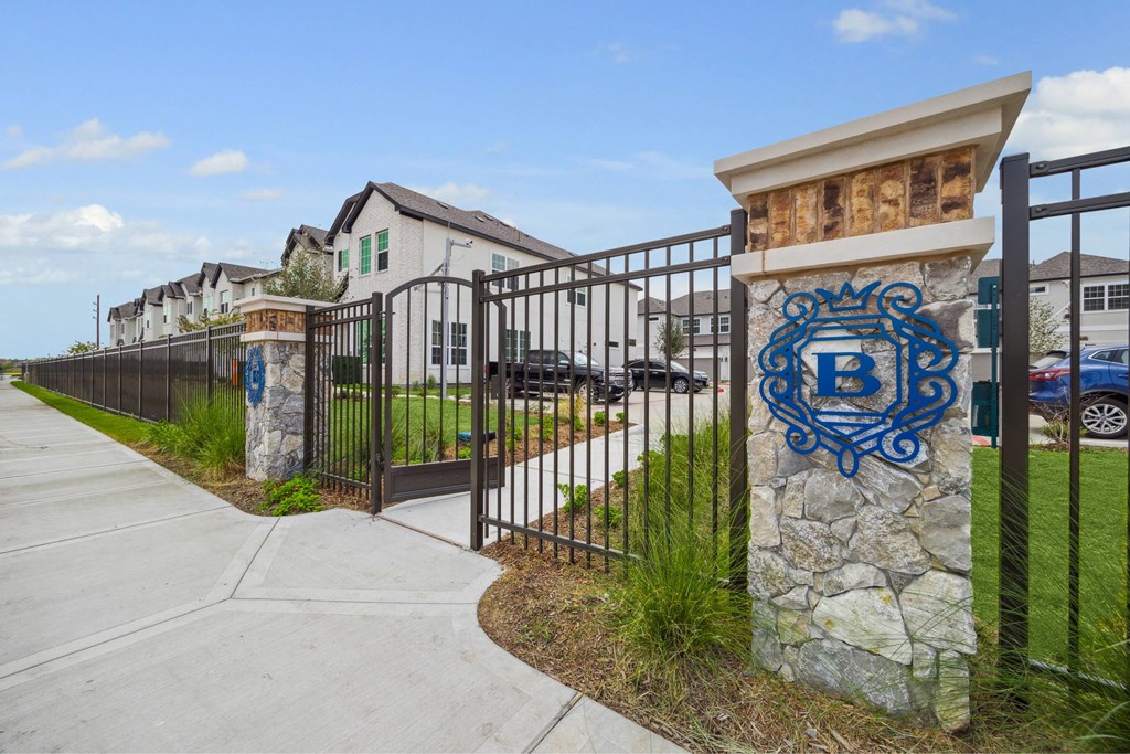 A gated community with a blue and white sign on a stone pillar.