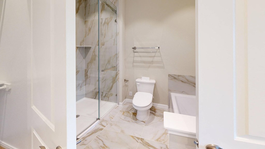 A white toilet sits in a bathroom with marble flooring and a glass shower door.