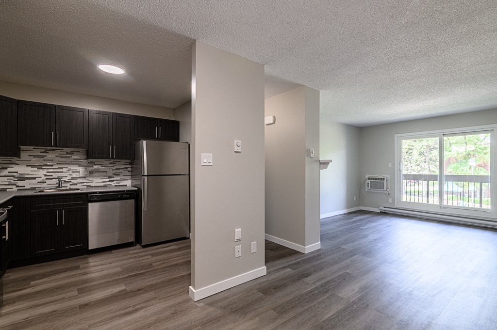 an empty living room with a kitchen in the background