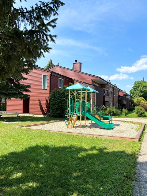A playground with a green slide and a red building in the background.