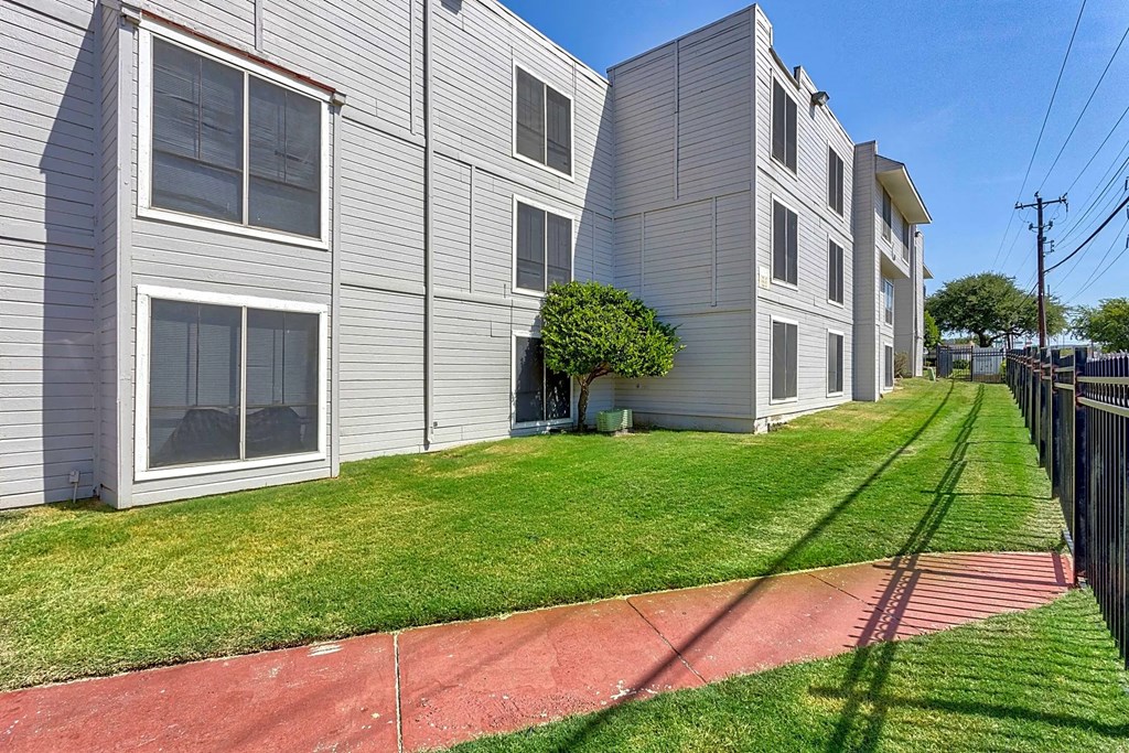 the front yard of an apartment building with grass and a sidewalk