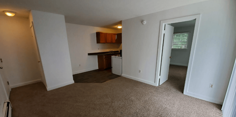 an empty living room with a kitchen in the background