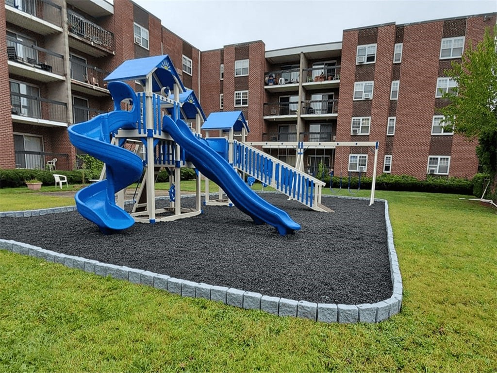 a playground with a blue playset in front of an apartment building