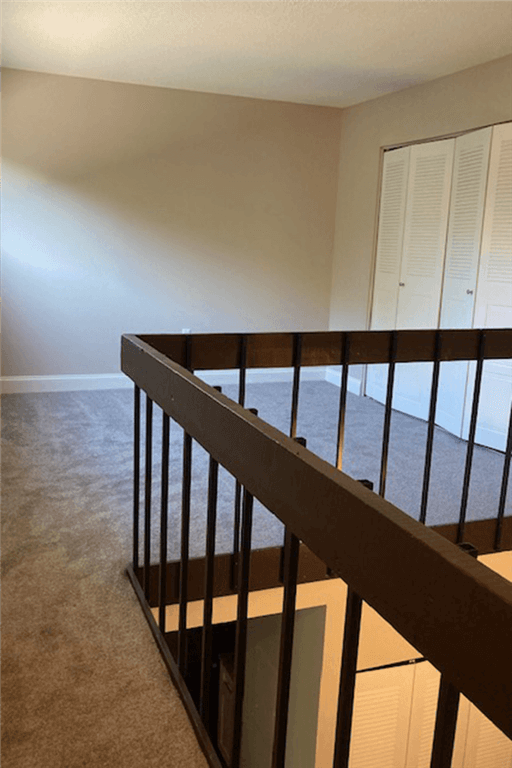 View of loft with grey carpet and wood railings at Silvertree Apartments