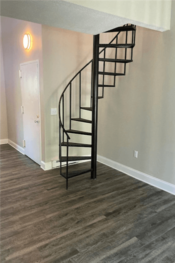 View of spiral staircase at Silvertree Apartments showing sand wood plank-style flooring and light tan walls - Photo Gallery 9