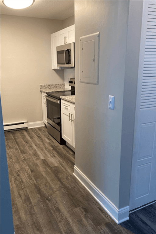 View of renovated kitchen at silvertree apartments showing grey plank-style flooring, white cabinets, and stainless steel appliances