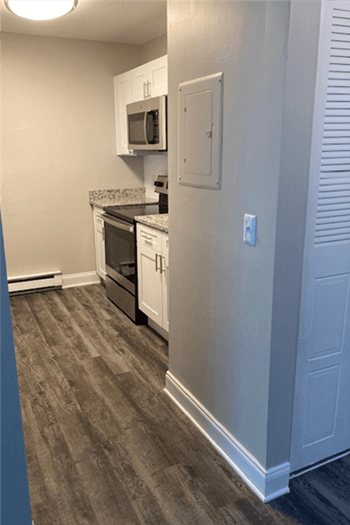 View of renovated kitchen at silvertree apartments showing grey plank-style flooring, white cabinets, and stainless steel appliances - Photo Gallery 15