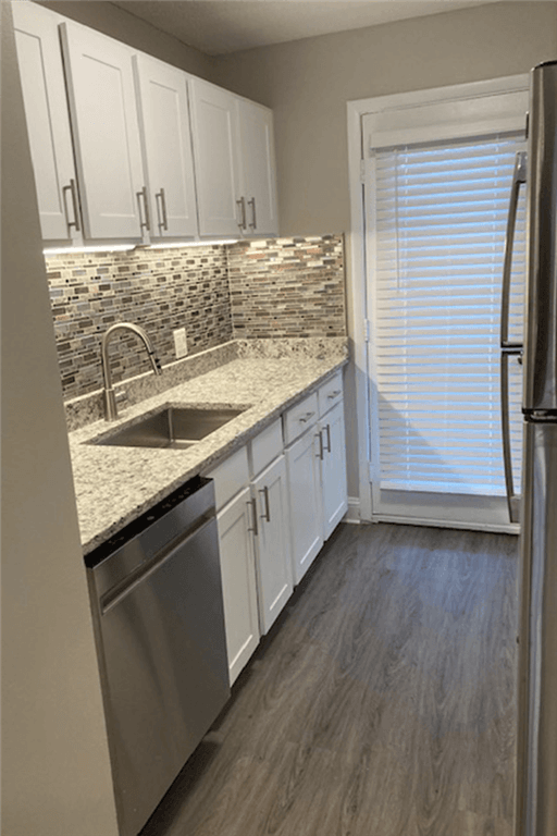 View of renovated kitchetwing white cabinets, grey plank-style flooring and granite countertops.