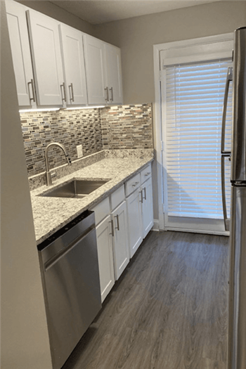 View of renovated kitchetwing white cabinets, grey plank-style flooring and granite countertops. - Photo Gallery 13