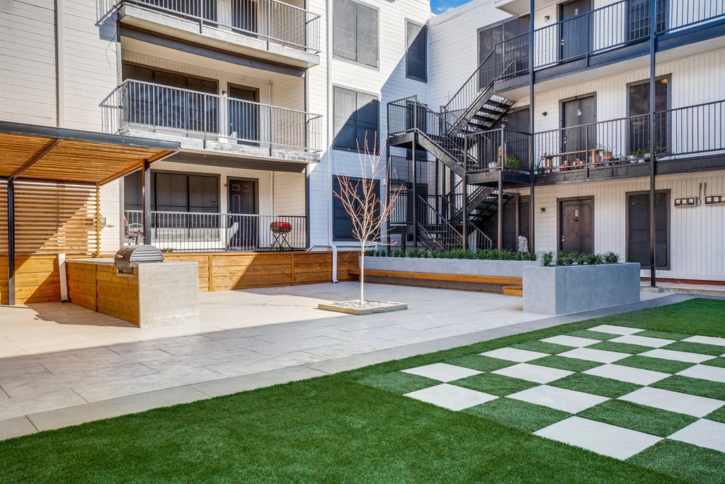 the yard of an apartment building with green grass and a checkerboard sidewalk