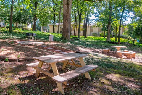 A wooden picnic table sits in a grassy area with trees in the background.
