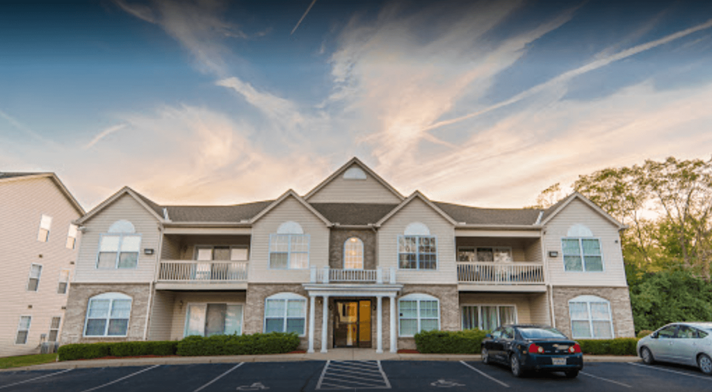 A large, well-lit apartment complex with multiple balconies and cars parked in the driveway.
