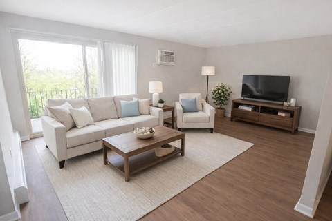 A living room with a white couch, a white chair, a wooden coffee table, and a television.