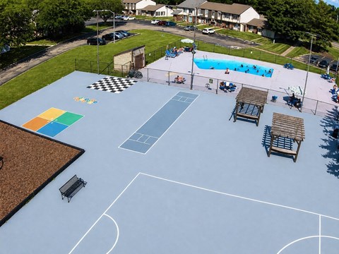 A basketball court with a blue surface and white lines, surrounded by a fence and with a pool in the background.