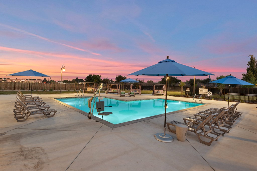 a swimming pool with chaise lounge chairs and umbrellas at dusk