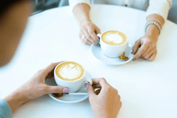 Two people are sitting at a table with cups of coffee.