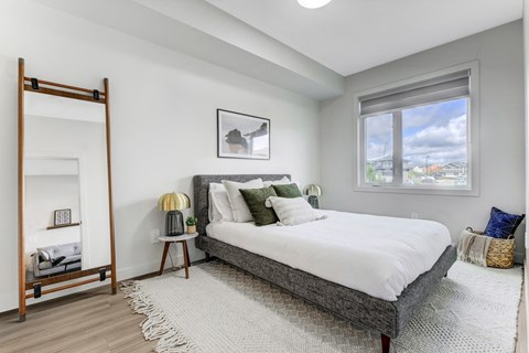 A bedroom with a large bed, a nightstand with a lamp, and a window with a view of the city.