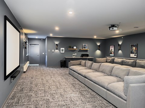 A spacious living room with a grey sofa and a large screen on the left side.