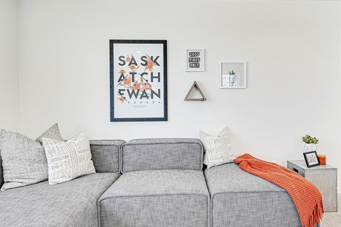 A grey couch with a red throw and a framed poster reading "Saskatchewan" on the wall behind it.