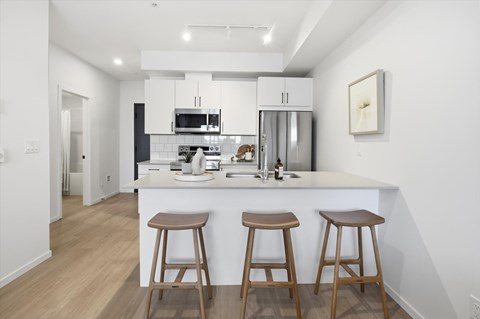 A kitchen with white cabinets and a white island with two stools.