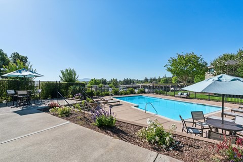 A pool surrounded by a patio with chairs and umbrellas.