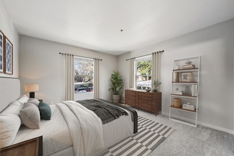 A bedroom with a large bed, a nightstand, and a window with a view of the street.