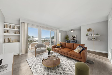 A living room with a brown sofa, a coffee table, and a large window with a view of the city.